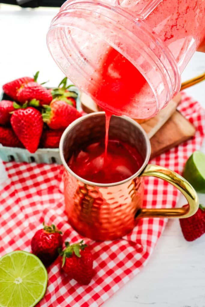 Strawberry puree being poured into a copper mug with ice.