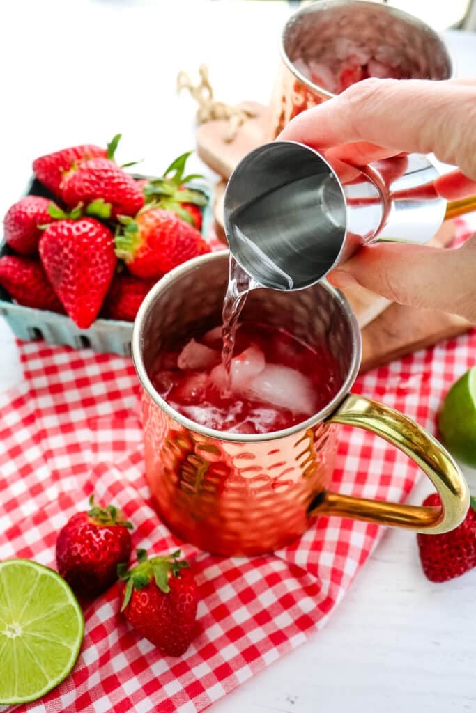 Shot of vodka being poured into a copper mug, with strawberries on the side and in the background.