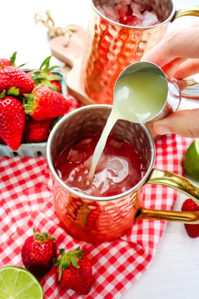 Lime juice being poured into a copper mug, with fresh strawberries and lime juice on the side.