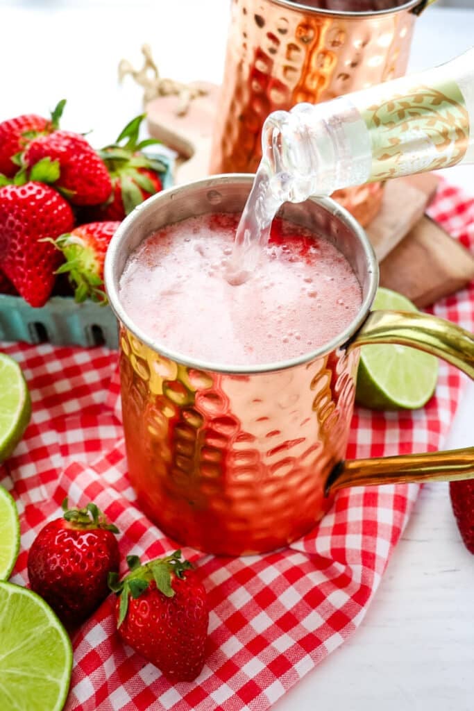 Ginger beer being poured into a copper mug to make a strawberry Moscow mule recipe.