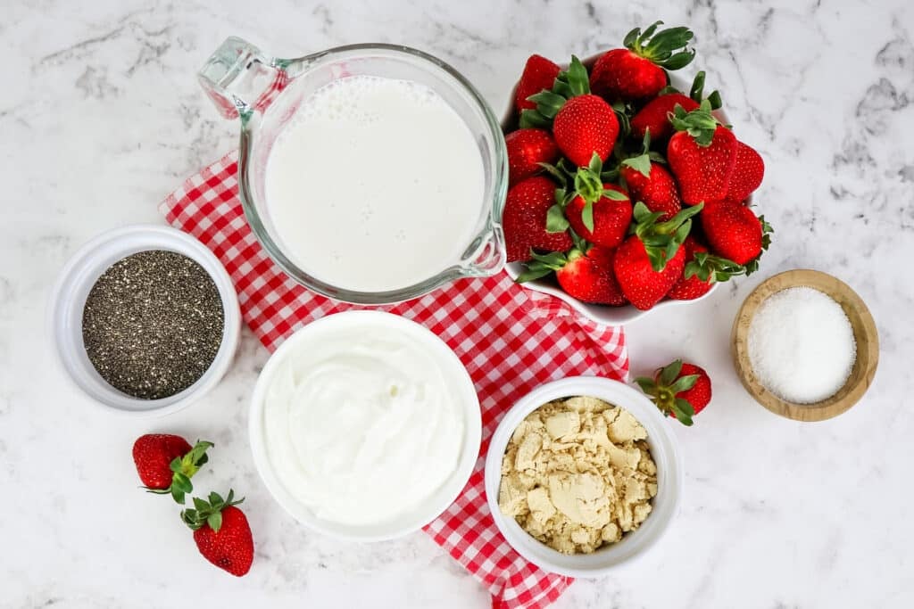 Ingredients needed to make strawberry chia seed pudding; strawberries, milk, protein powder, Greek yogurt, chia seeds and sweetener.
