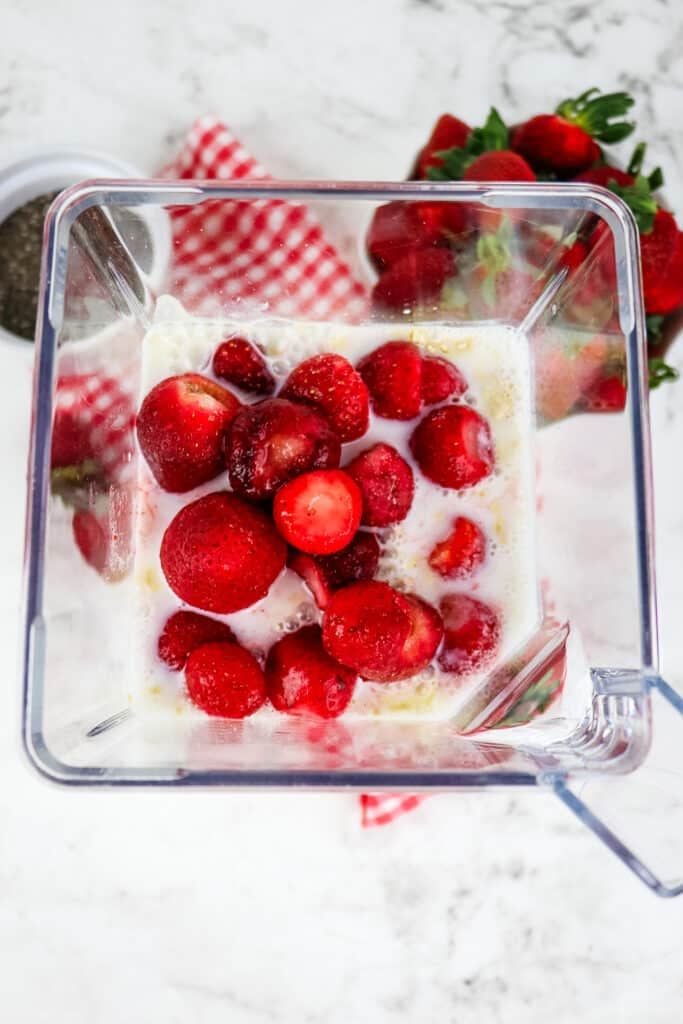 Strawberries, milk, yogurt and protein powder in a blender jar before being blended.