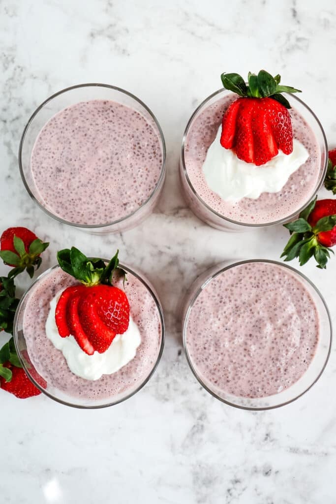 Strawberry chia seed pudding in round containers topped with Greek yogurt and fresh sliced strawberries.