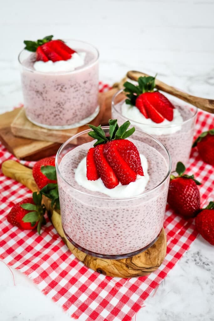 Strawberry chia pudding in three round glass bowls topped with Greek yogurt and sliced fresh strawberries.