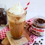 Nutella iced coffee topped with whipped cream and straw with jar of Nutella off to the side.