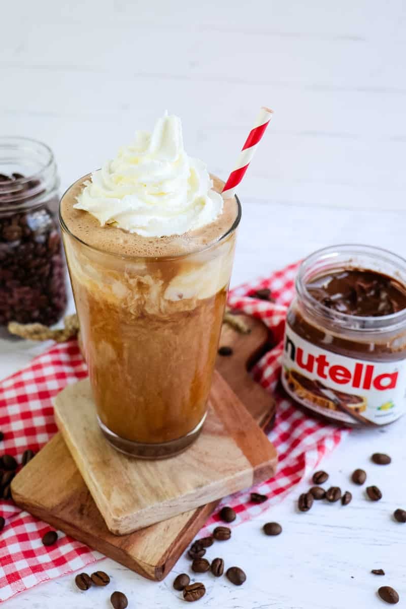 Nutella iced coffee topped with whipped cream and straw with jar of Nutella off to the side.