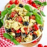 Tortellini pasta salad with pesto garnished with fresh basil leaves in a bowl.