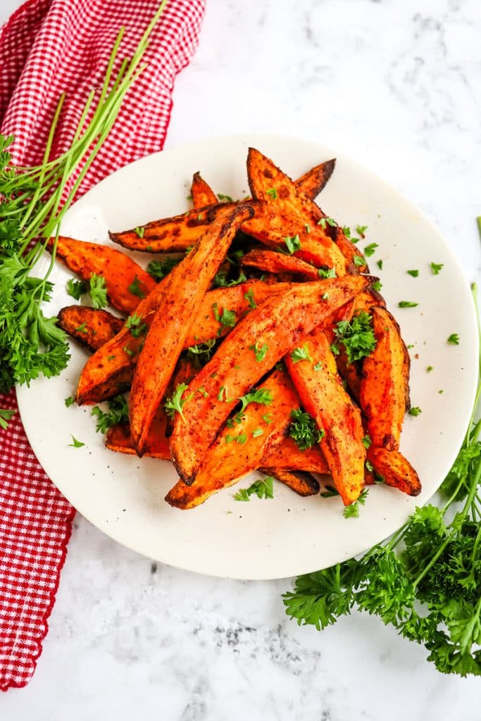 Air fryer sweet potato wedges on a plate topped with chopped parsley.