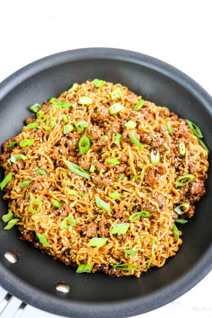 Mongolian beef noodles in a skillet topped with sliced green onions and sesame seeds.