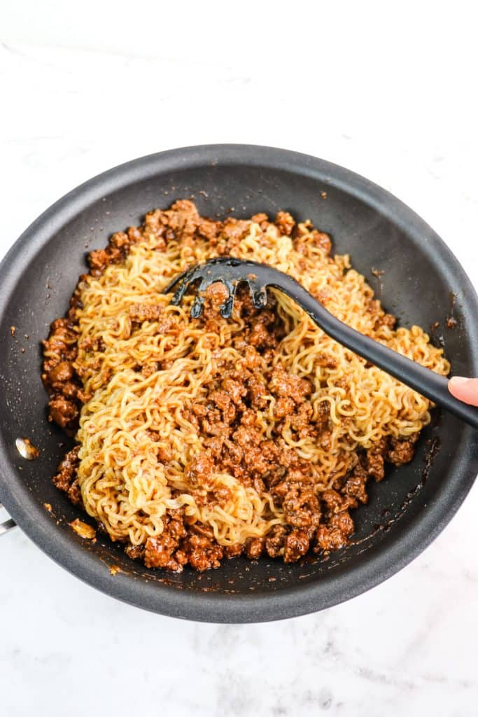 Ground beef and ramen noodles mixed together in a skillet with a utensil.