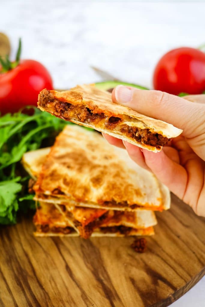 A stack of beef quesadilla tacos with one slice held in hand.