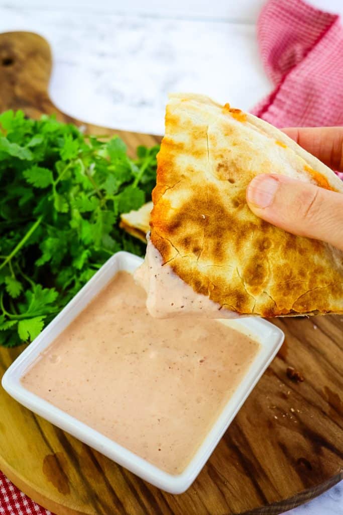 A slice of beef quesadilla being dipped in sauce.