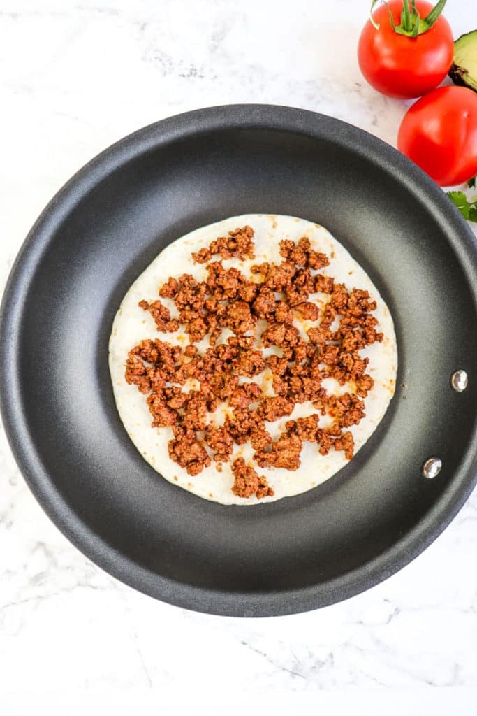 A tortilla topped with ground beef in a skillet for a quesadilla taco.