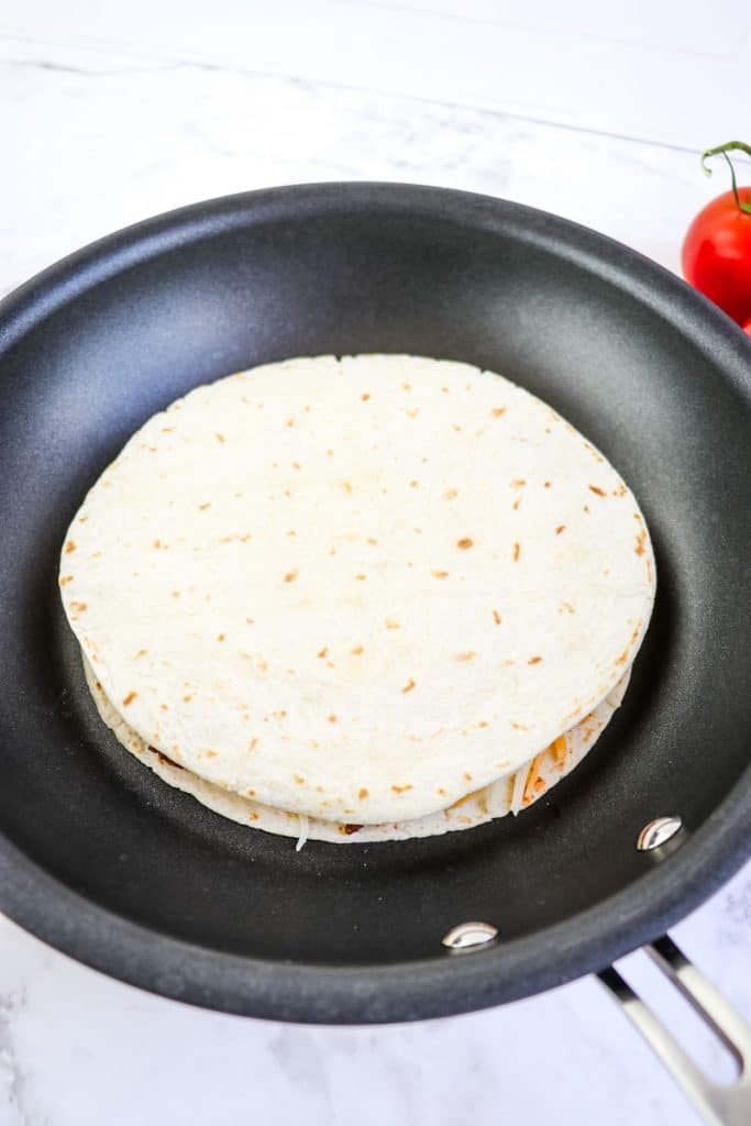 A beef quesadilla topped with a flour tortilla in a skillet.