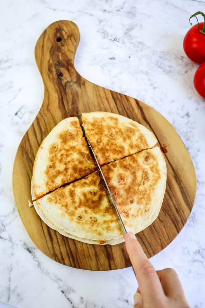 A quesadilla taco on a cutting board being cut into quarters with a knife.