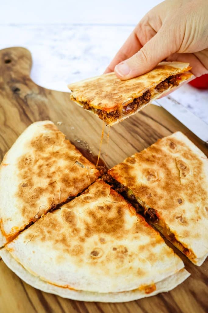 A ground beef quesadilla cut into four quarters with one slice being held in hand.