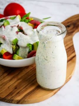 Yogurt dill dressing in a tall bottle with dressed salad in the background.