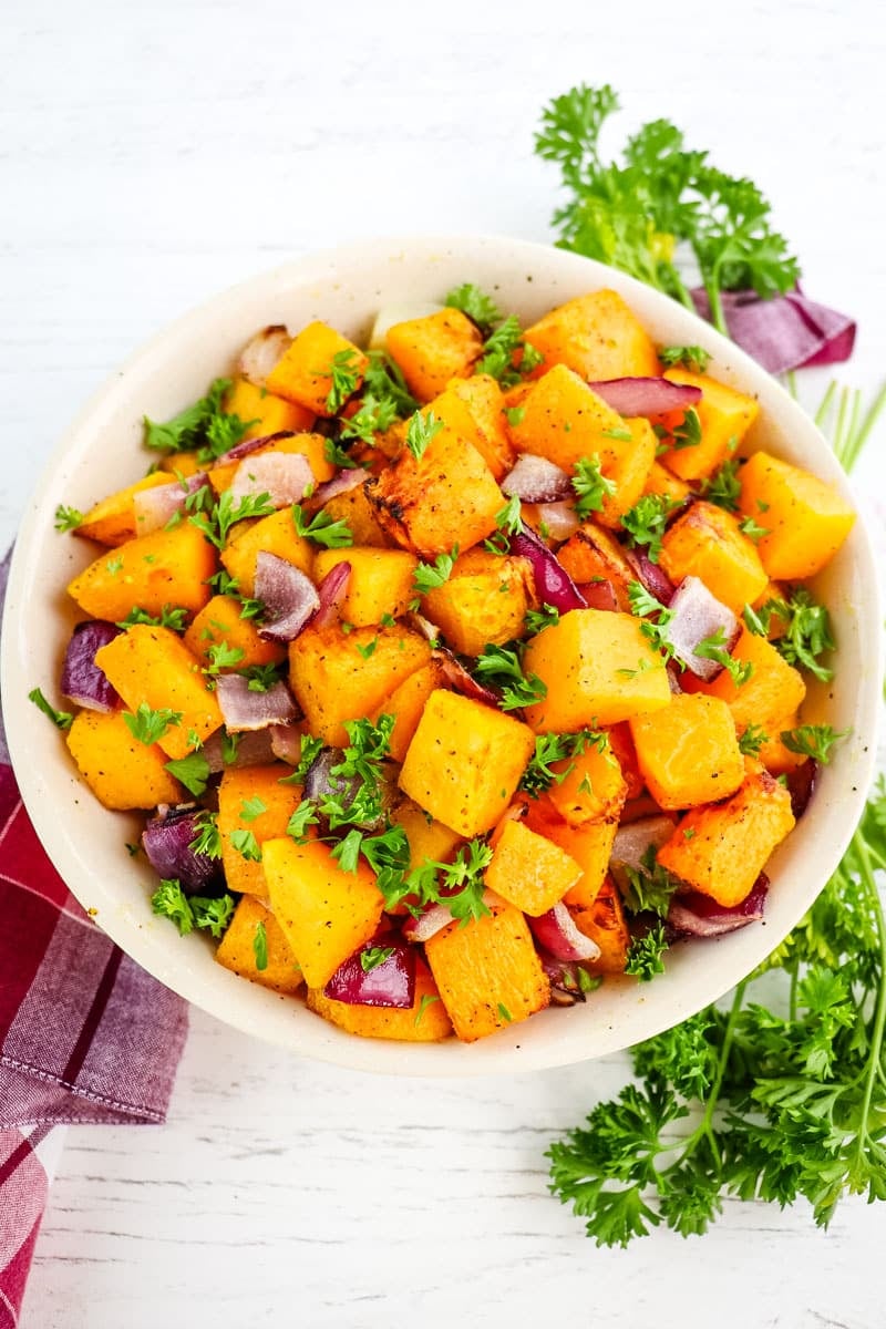 Bowl of seasoned air fryer butternut squash with red onion and minced parsley.