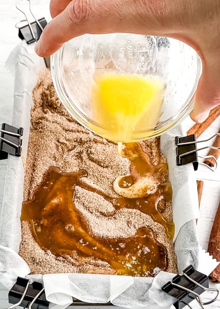 Melted butter being poured over the top of cinnamon swirl bread.