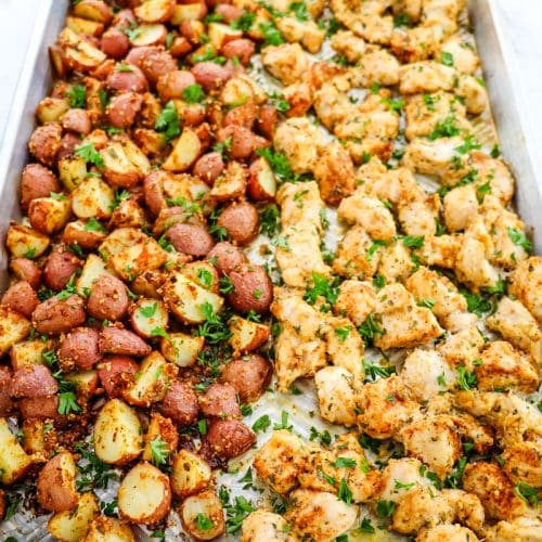 Garlic parmesan chicken and red potatoes on a sheet pan topped with chopped parsley.