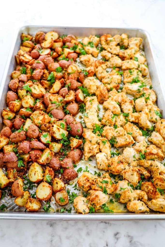 Garlic parmesan chicken and red potatoes on a sheet pan topped with chopped parsley.