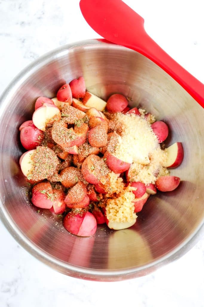 Red potatoes in a mixing bowl with spices, garlic and parmesan cheese.