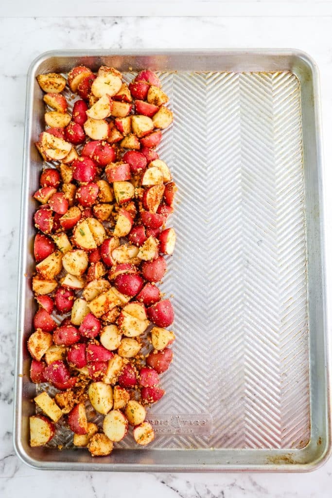 Seasoned red potatoes on one side of a sheet pan before going into the oven. 