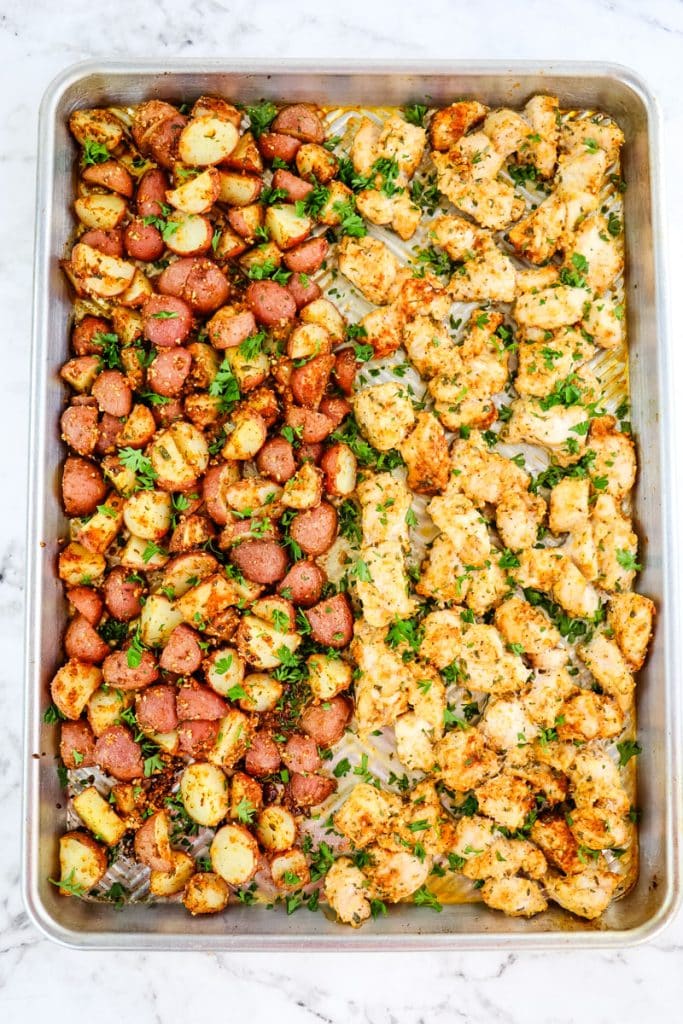 Baked garlic parmesan chicken and potatoes on a sheet pan topped with chopped parsley.