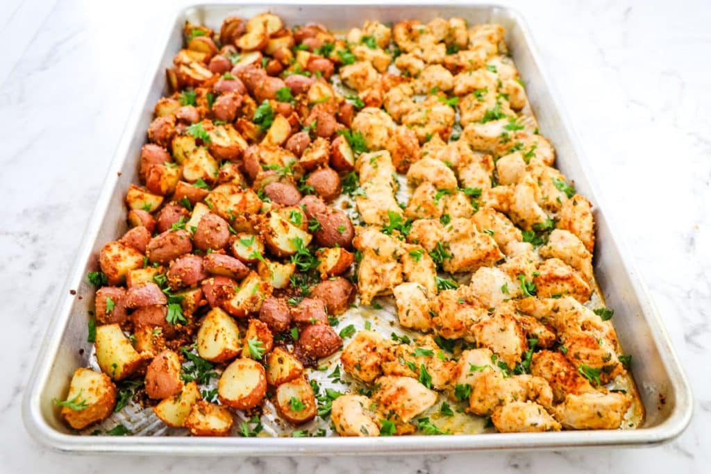Baked garlic parmesan chicken and potatoes on a sheet pan topped with chopped parsley.