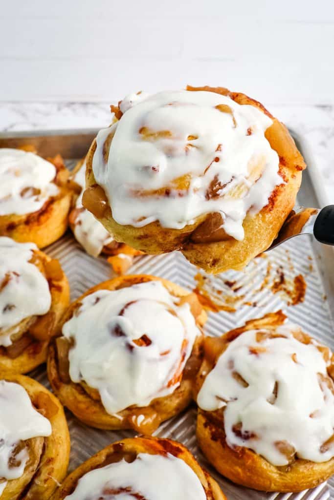 Cinnamon roll being lifted off the pan with a spatula.