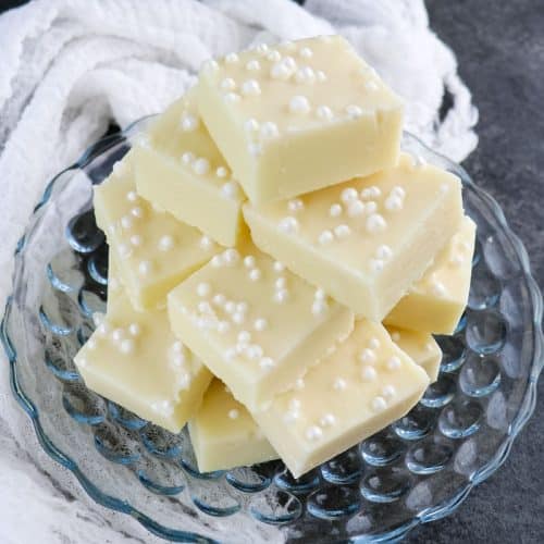 Squares of vanilla fudge stacked on a glass plate.