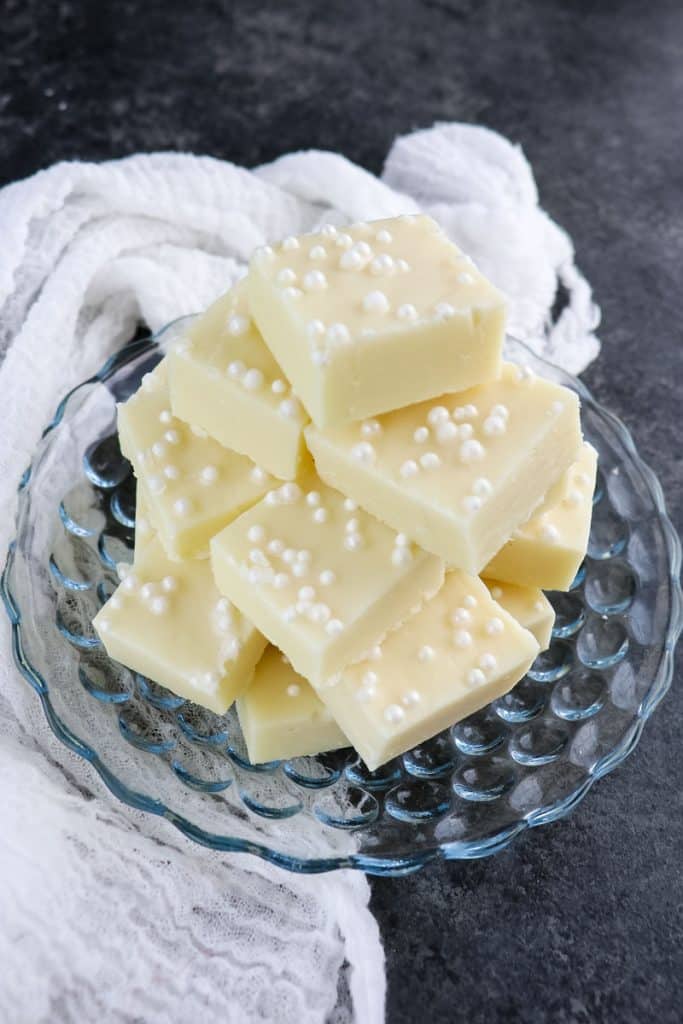 Squares of vanilla fudge stacked on a glass plate.