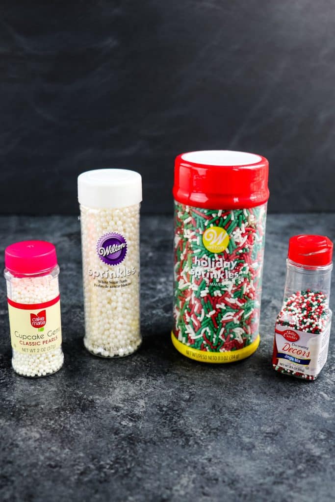 Two containers of white pearl sprinkles and two containers of red and green Christmas sprinkles.