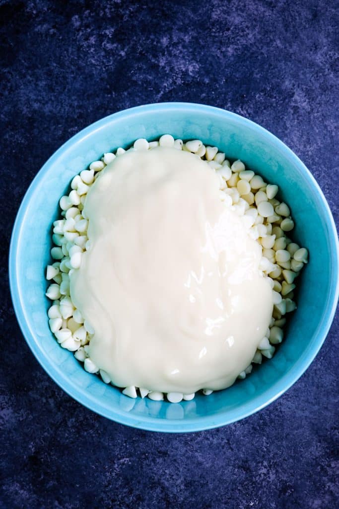 White chocolate chips and sweetened condensed milk in a light blue bowl.