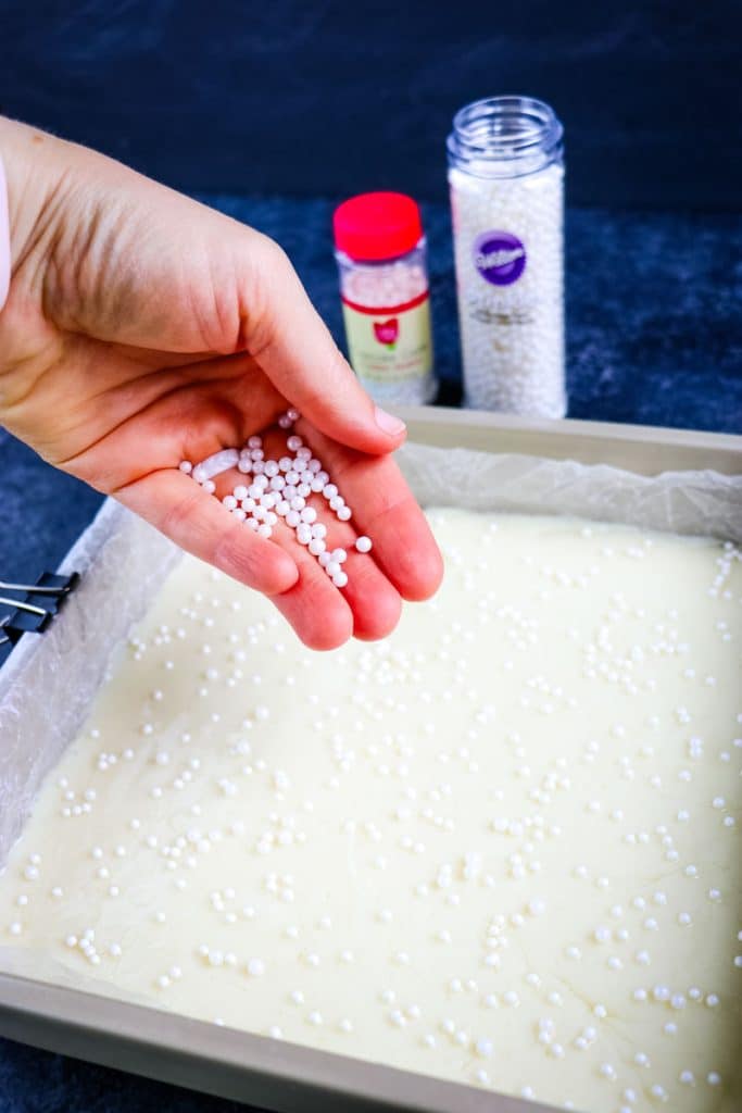 White pearl sprinkles being added to the vanilla fudge in the pan.