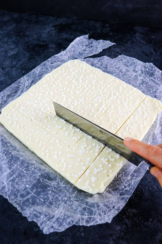 White chocolate fudge being cut into squares with a large knife.