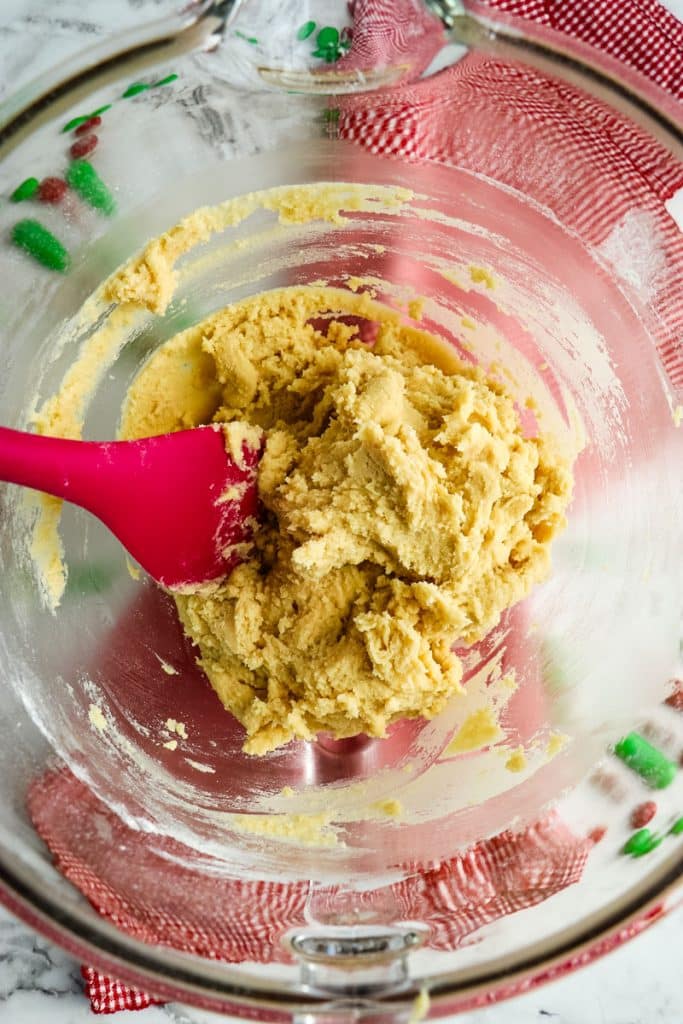 Cookie dough in a mixing bowl with a red rubber scraper in the center.