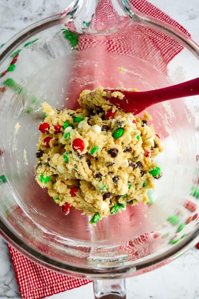 Cookie dough mixed together with chocolate chips and M&M's in a mixing bowl.