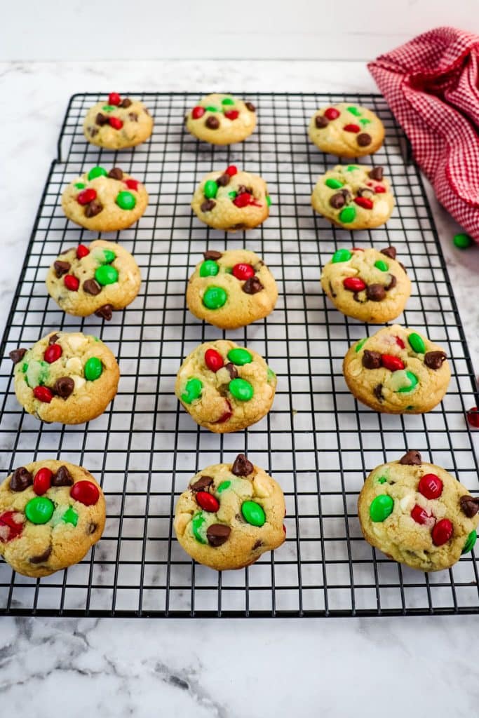 Baked M&M Christmas cookies on a cooling rack, topped with chocolate chips and M&M's.