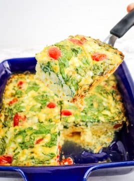 Cottage cheese egg bake with spinach and tomatoes, with slice being lifted out of baking dish.