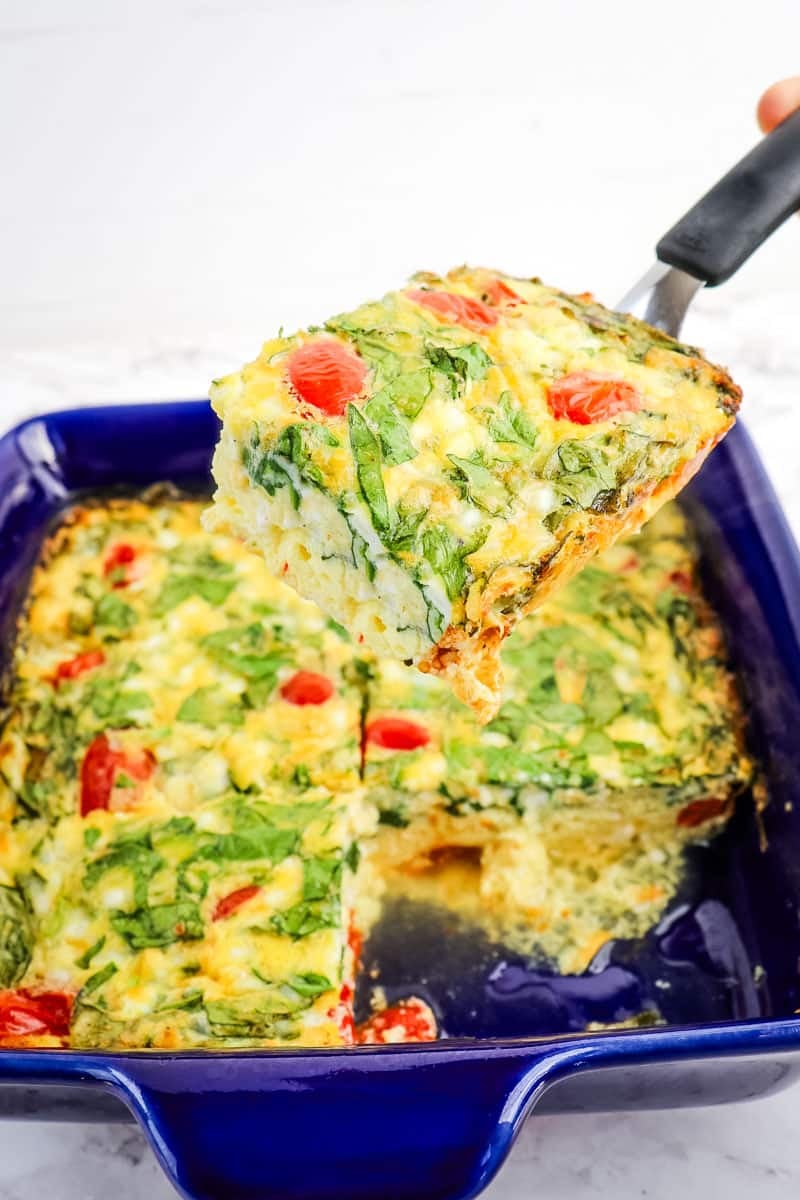 Cottage cheese egg bake with spinach and tomatoes, with slice being lifted out of baking dish.