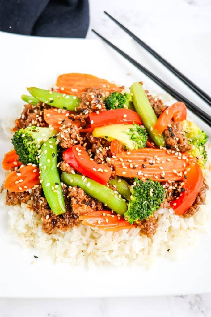 Ground beef stir fry with vegetables served over rice and topped with sesame seeds.