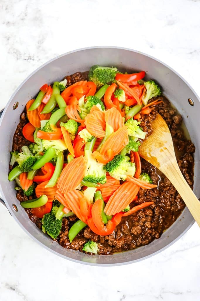 Seasoned ground beef and steamed vegetables in a large skillet for ground beef stir fry.