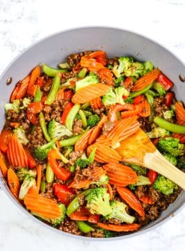 Ground beef stir fry with steamed vegetables stirred together with a wooden spoon.
