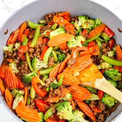 Ground beef stir fry with steamed vegetables stirred together with a wooden spoon.