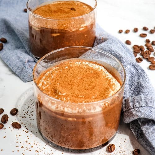 Two jars of tiramisu overnight oats topped with vanilla Greek yogurt and cocoa powder.