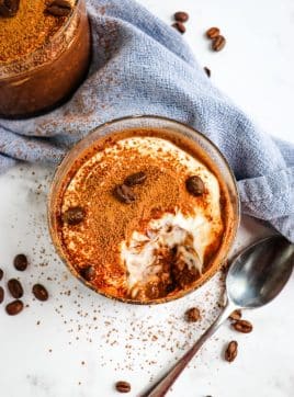 Top down look of the tiramisu overnight oats topped with cocoa powder and garnished with coffee beans; bite taken out to see the layers of the oats.