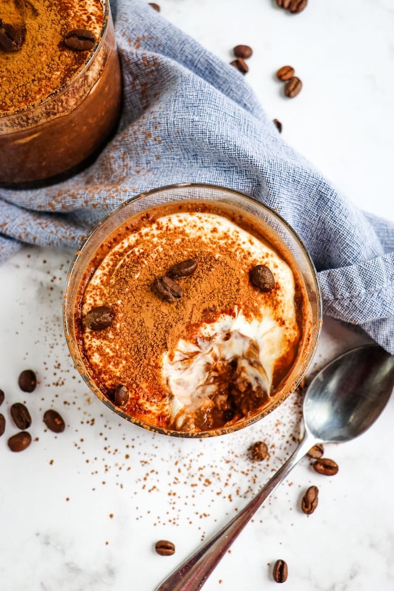 Top down look of the tiramisu overnight oats topped with cocoa powder and garnished with coffee beans; bite taken out to see the layers of the oats.