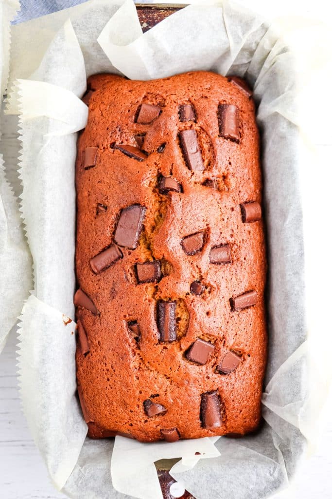 Whole loaf of chocolate chunk banana bread in parchment paper lined pan.