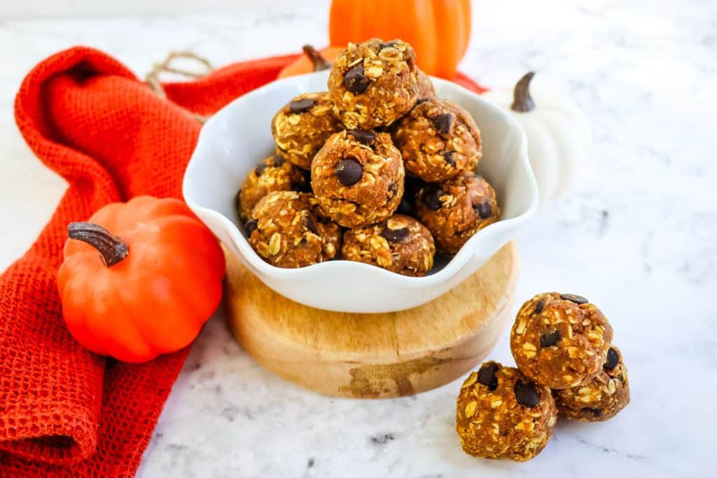 Pumpkin chocolate chip protein balls in a white bowl with pumpkins in the background.